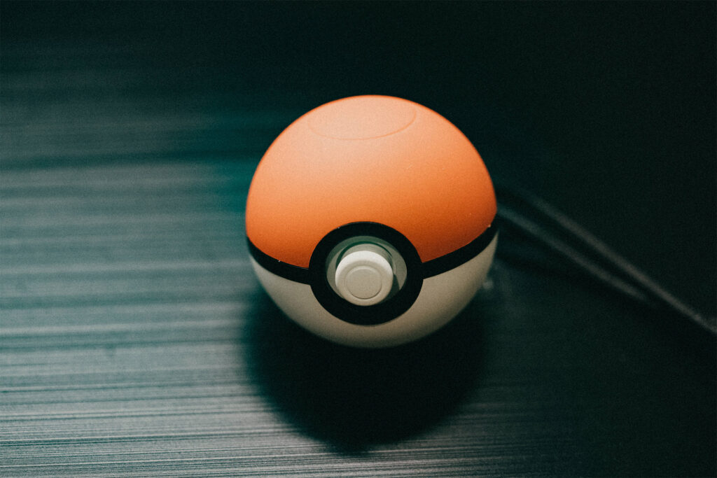 Eine Nahaufnahme eines Pokéballs, des ikonischen Geräts, mit dem Pokémon wie Charizard gefangen werden können, das auf einer dunklen, strukturierten Oberfläche liegt.