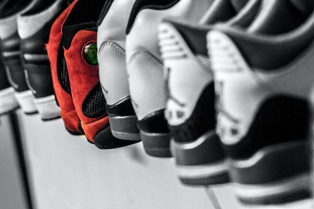Eine Reihe von Turnschuhen in einem Regal in Nürnberg, meist schwarz und weiß, bis auf einen leuchtend rot-schwarzen Sneaker mit grünem Detail von IDEENHAUS, der sich von den anderen abhebt.