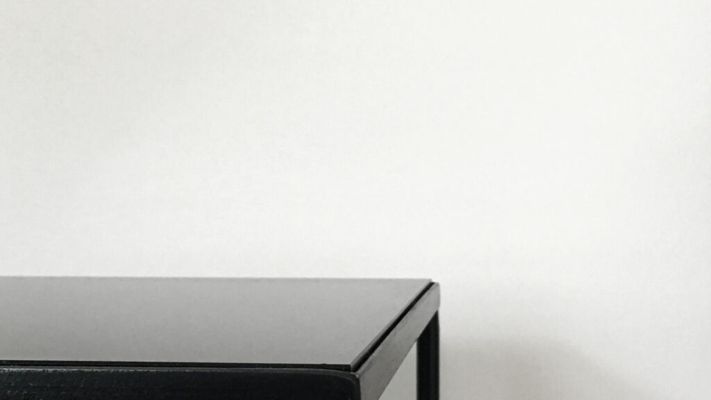 Nahaufnahme der oberen Ecke eines schwarzen, minimalistischen Tisches oder Regals vor einem schlichten weißen Hintergrund, der klare Linien und ein modernes Design zeigt.