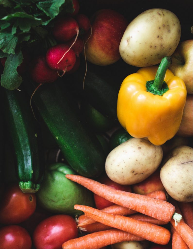 Eine bunte Auswahl an frischem Gemüse - Karotten, Kartoffeln, Zucchini, gelbe Paprika, Radieschen, Tomaten - und ein Apfel sind dicht beieinander angeordnet, ideal für jeden Ernährungsbericht, der auf gesunde Ernährung ausgerichtet ist.