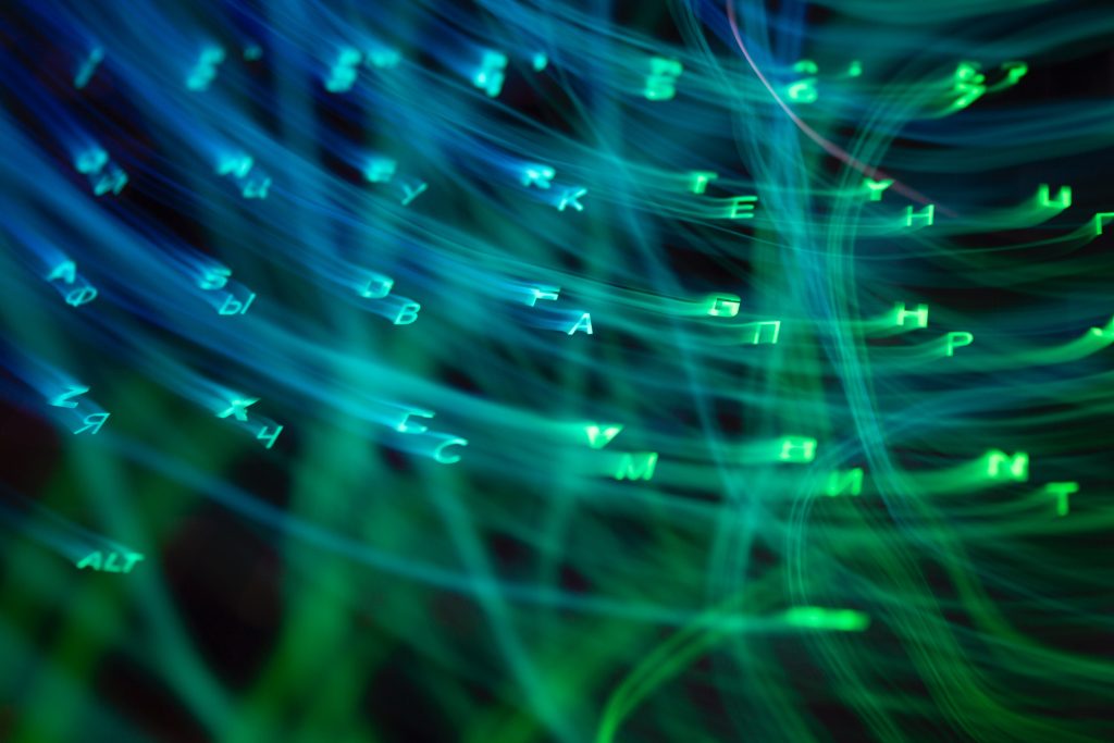 Leuchtend grüne und blaue Buchstaben und Symbole, inspiriert von ai, schweben über einen dunklen Hintergrund mit wirbelnden Lichtspuren und schaffen eine digitale, futuristische Atmosphäre.