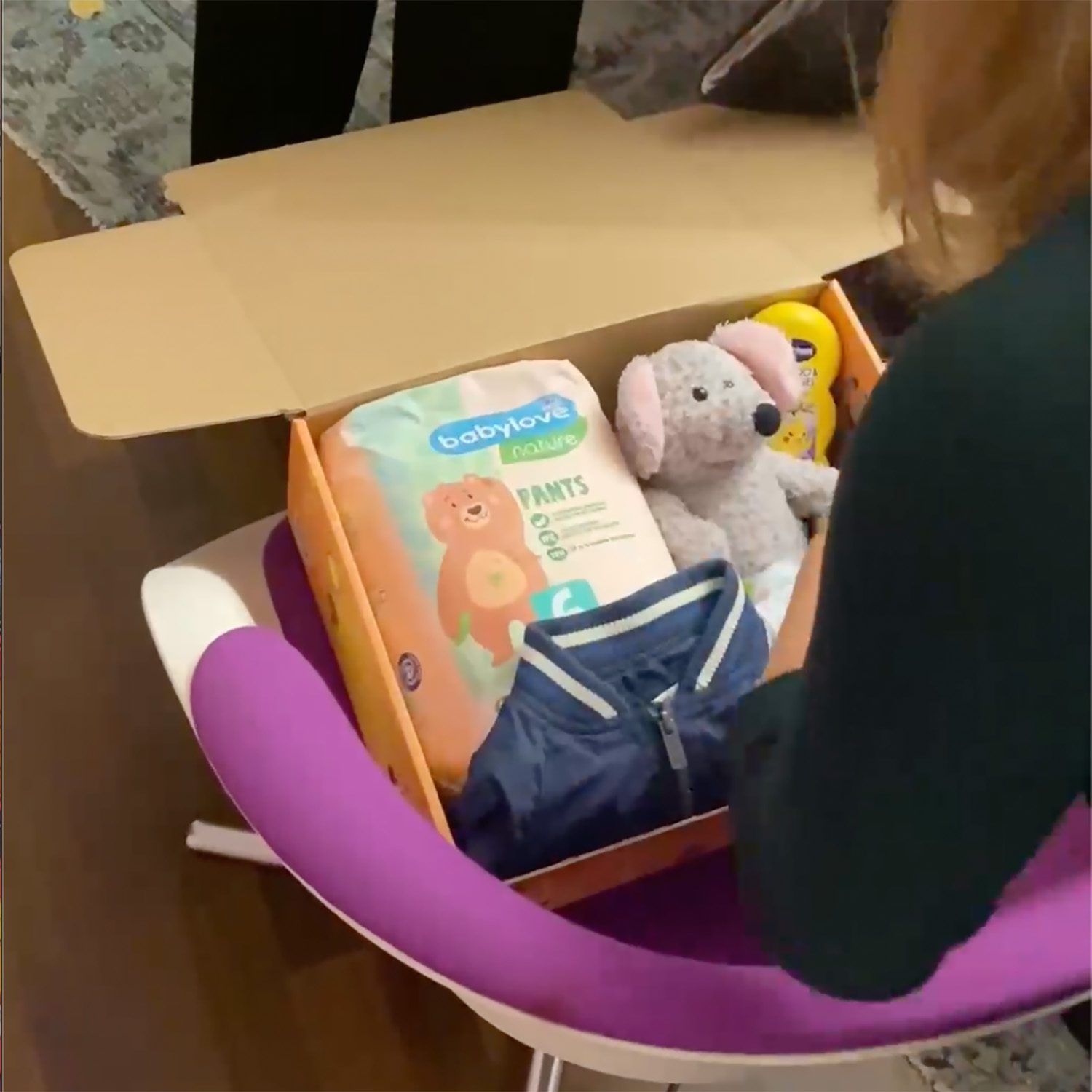 Eine Person packt eine Schachtel mit Babyartikeln - darunter Babylove-Windeln, Spielzeug und eine blaue Jacke