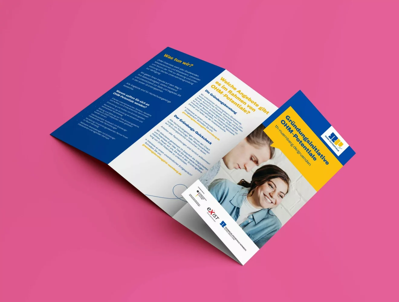 Eine dreifach gefaltete Broschüre auf einer rosafarbenen Oberfläche mit blauen, weißen und gelben Feldern mit deutschem Text, Logos und einem Foto von zwei lächelnden Frauen, die zusammen lesen.